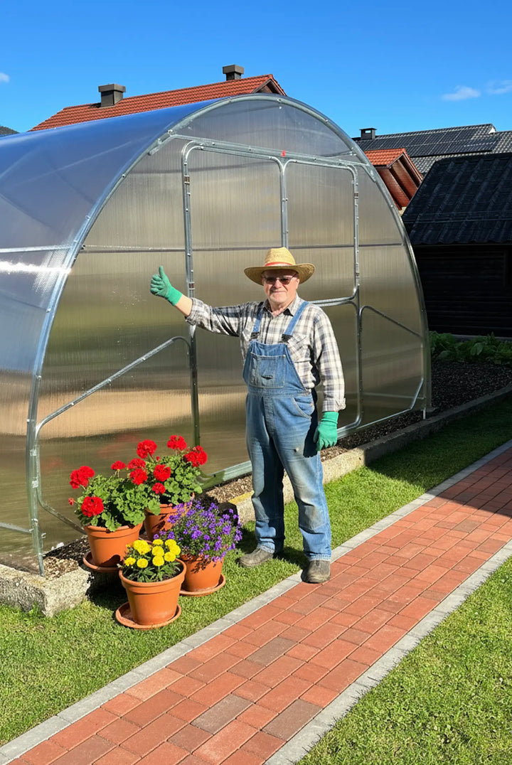 Gardener beside a 3m polycarbonate greenhouse, showing scale and build quality, with potted flowers in front.