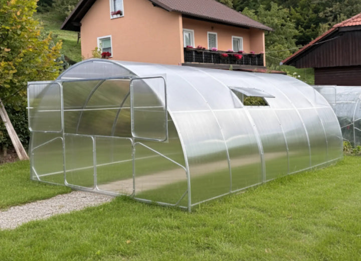 3m polycarbonate greenhouse with arched frame and roof vent, shown installed in a garden beside a house.
