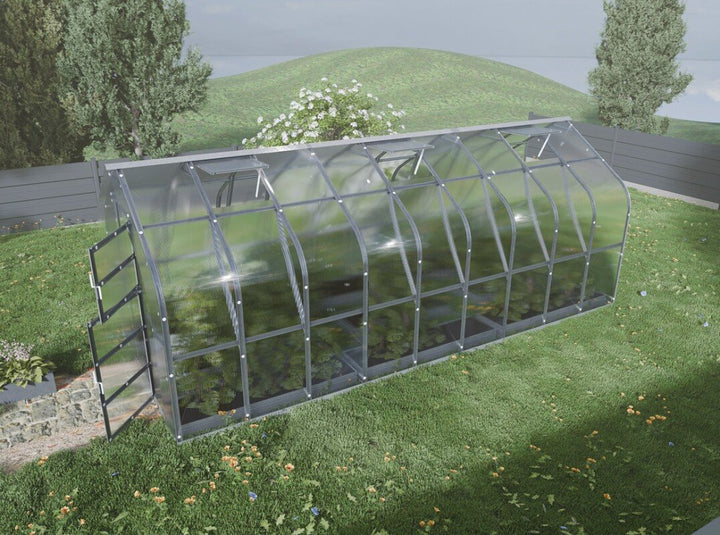 Greenhouse on a grassy area with trees and a road in the background