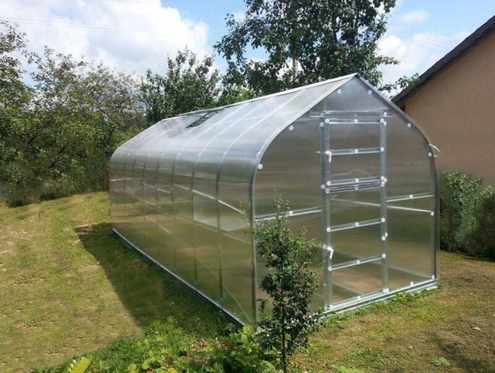 Polycarbonate greenhouse on a grassy area with trees in the background